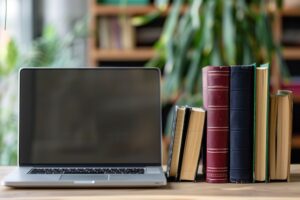 A laptop sits on a desk next to a stack of textbooks, symbolizing the modern methods of learning.